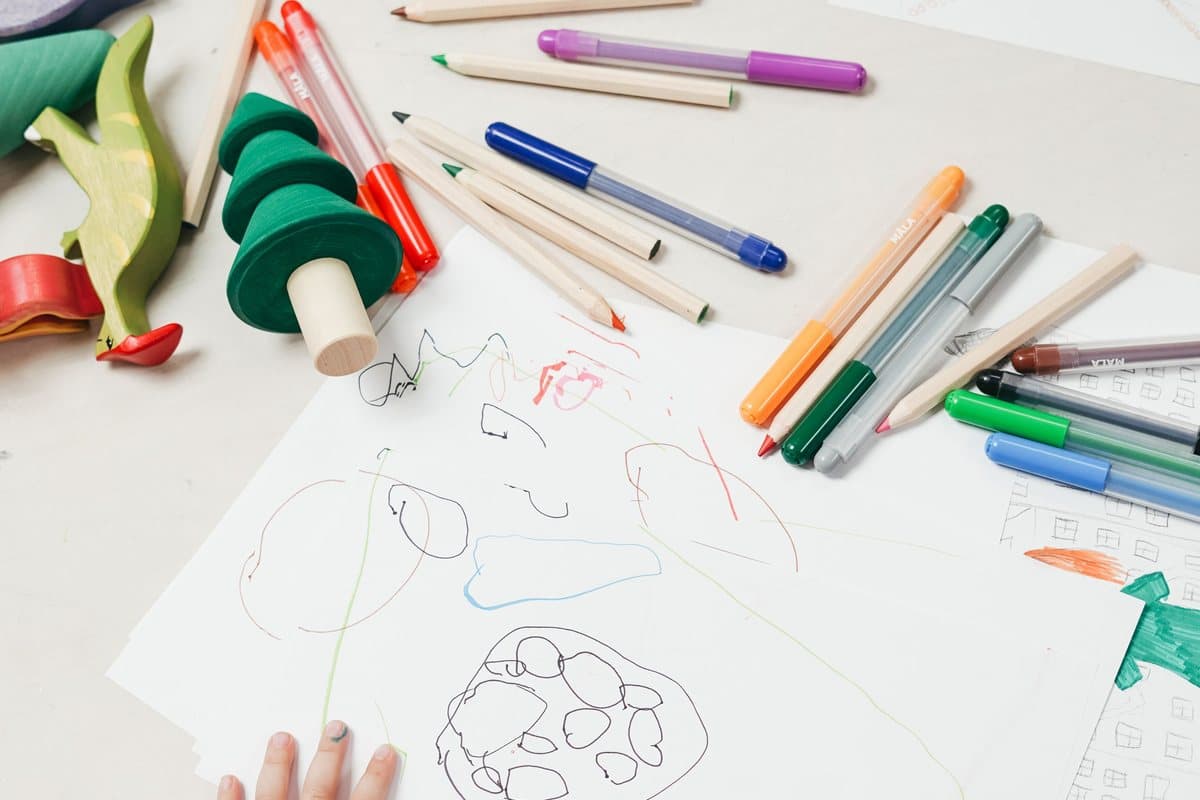 Enfant dessinant aux feutres entouré de jouets en bois